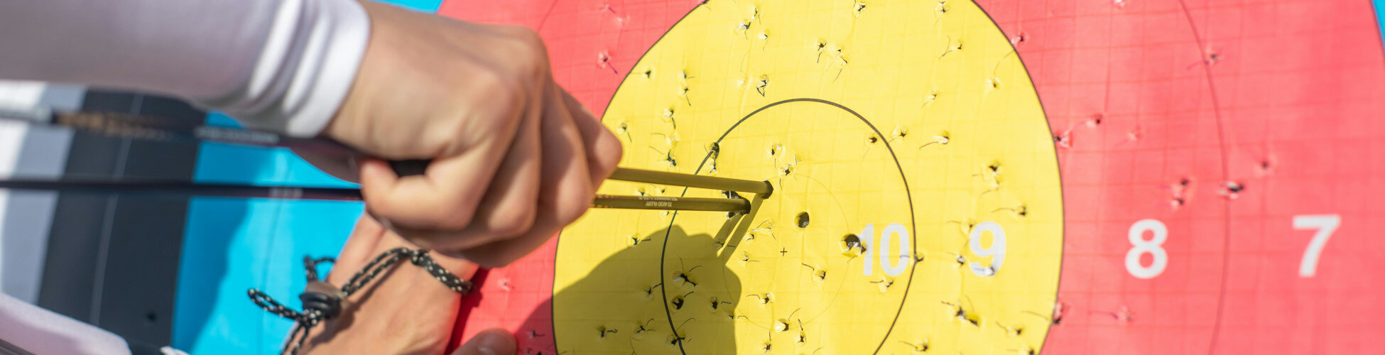 Close-up of an archer pulling a tight group of arrows from the center of a yellow and red target face.