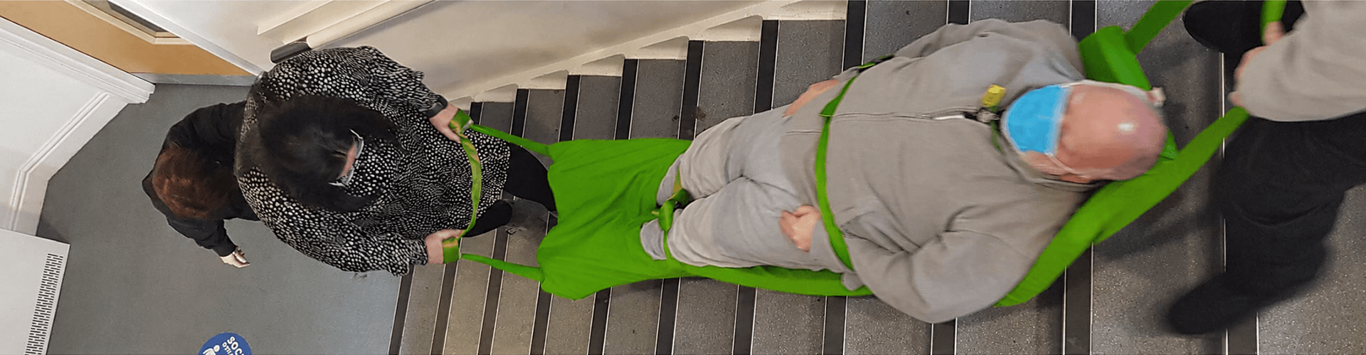 Healthcare workers practicing a controlled staircase descent using a red emergency evacuation sledge during a practical safety compliance course in Cheshire.