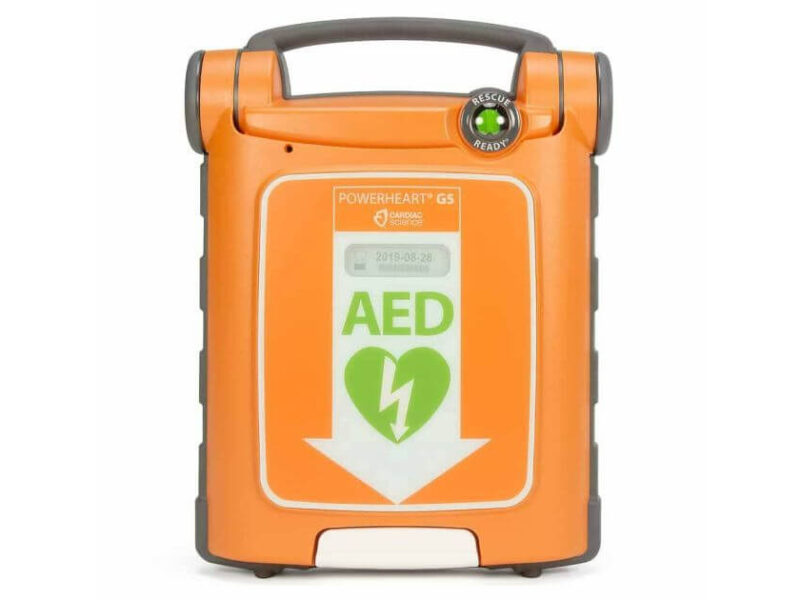 An orange and grey Cardiac Science Powerheart G5 automated external defibrillator (AED) shown against a clean white background, displaying its green rescue ready indicator status button and central green heart safety icon.